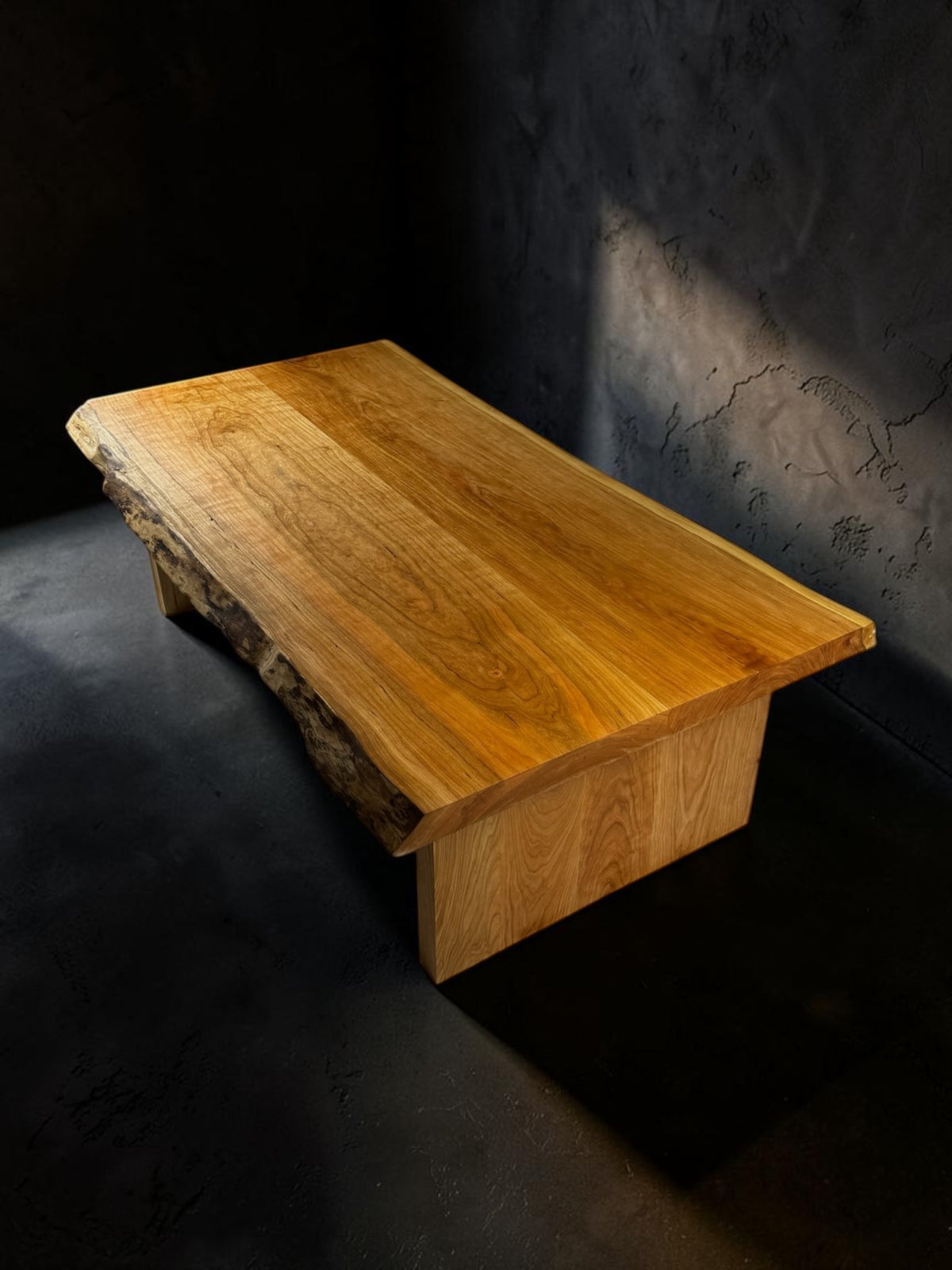 Light solid wood live edge coffee table on a dark studio background
