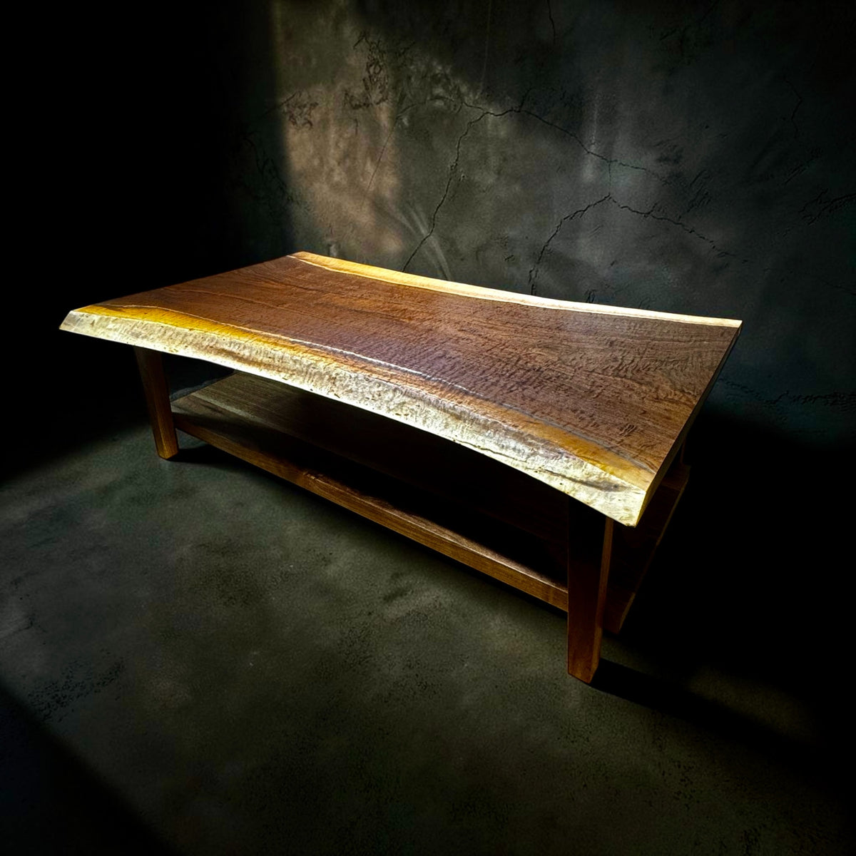 Live edge solid wood coffee table with lower shelf on a dark studio background